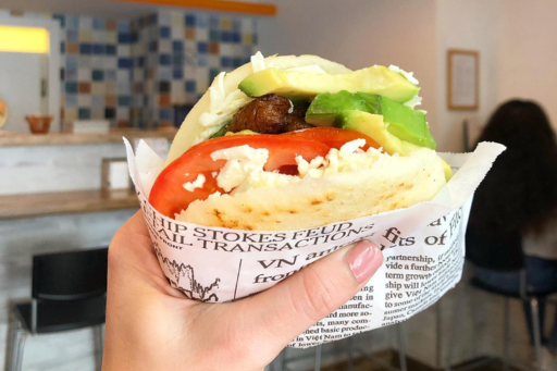 A hand holding an arepa filled with avocado and tomato