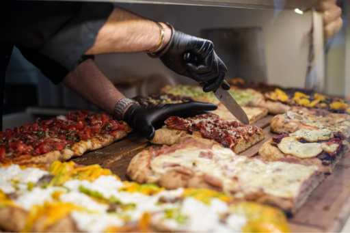 A person cutting a slice of pizza on a stand