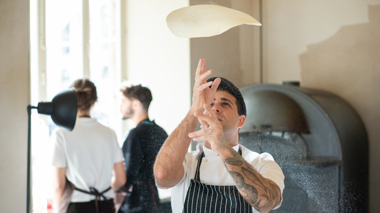 a man in an apron throwing a pizza dough into the air